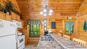Una cucina in legno con piano di lavoro in granito, un frigorifero, un fornello, un lavello e un lampadario.