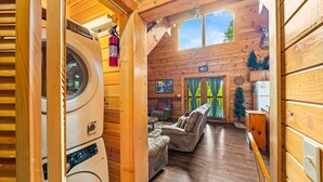 Accogliente interno di una baita con lavatrice, camino, zona pranzo e vista sull'esterno.