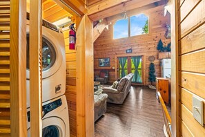 A cozy cabin interior with a washing machine, a fireplace, a dining area, and a view of the outdoors.