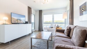 Una sala de estar moderna con un televisor de pantalla plana, un sofá, una mesa de centro y vistas al exterior.