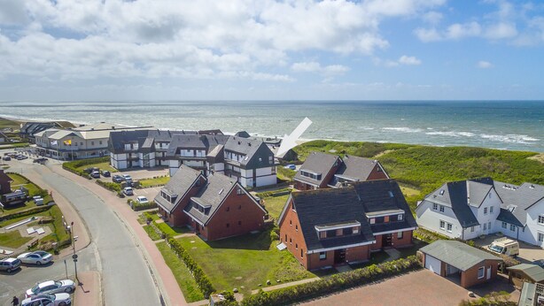 Zona residencial costera con casas, una calle y el mar al fondo.