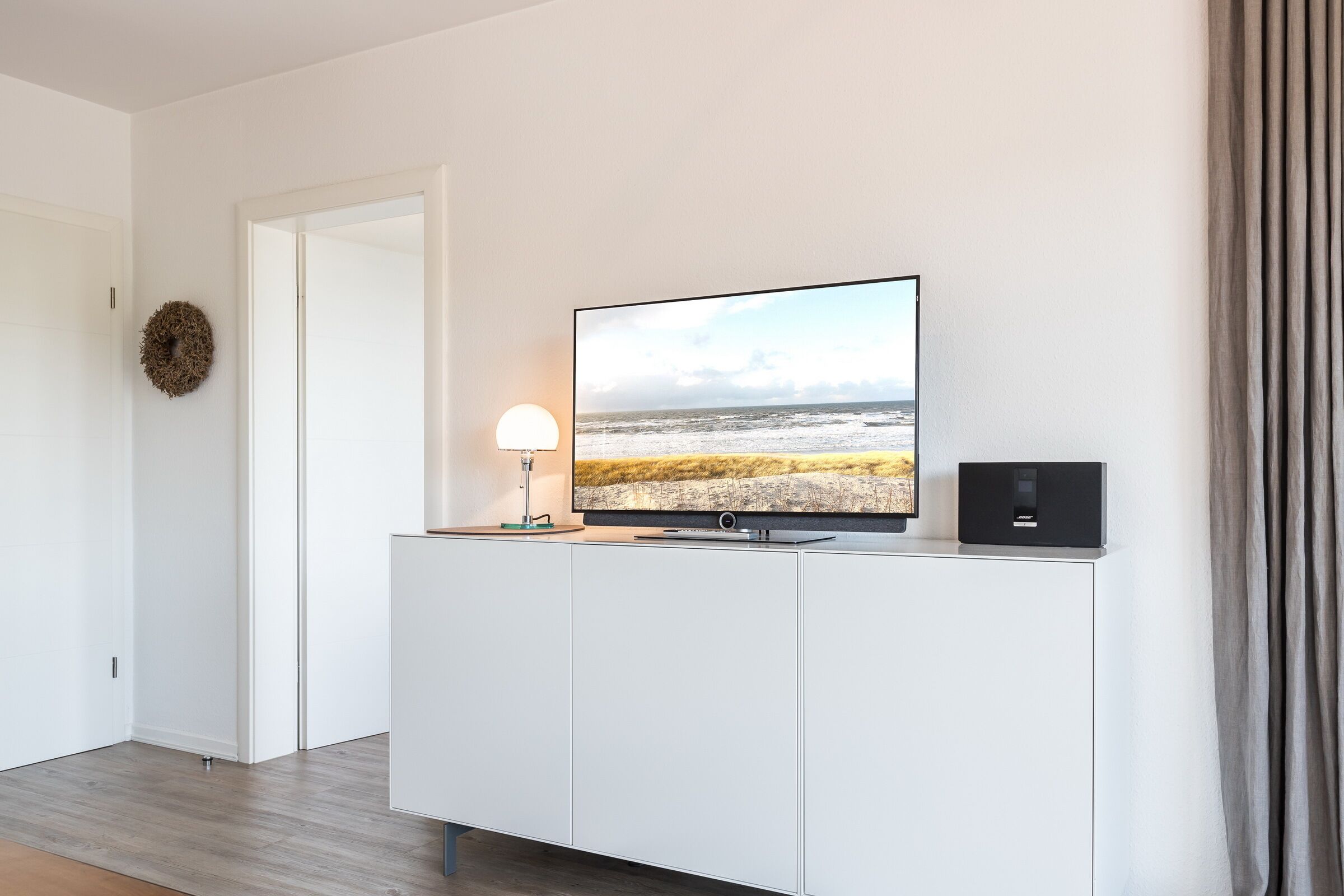 Ein modernes Wohnzimmer mit Flachbildfernseher auf einem weißen Schrank, einer Lampe und einer Stereoanlage.