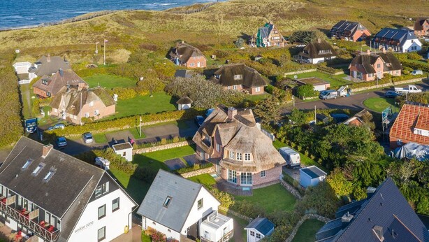 A coastal village with houses, some with thatched roofs, and a view of the sea. - Düne 22 - Wohnen Unter Reet (Wenningstedt-Braderup (Sylt))