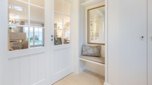 A hallway with a white door, a bench with a cushion, and a mirror on the wall. - Düne 22 - Wohnen Unter Reet (Wenningstedt-Braderup (Sylt))