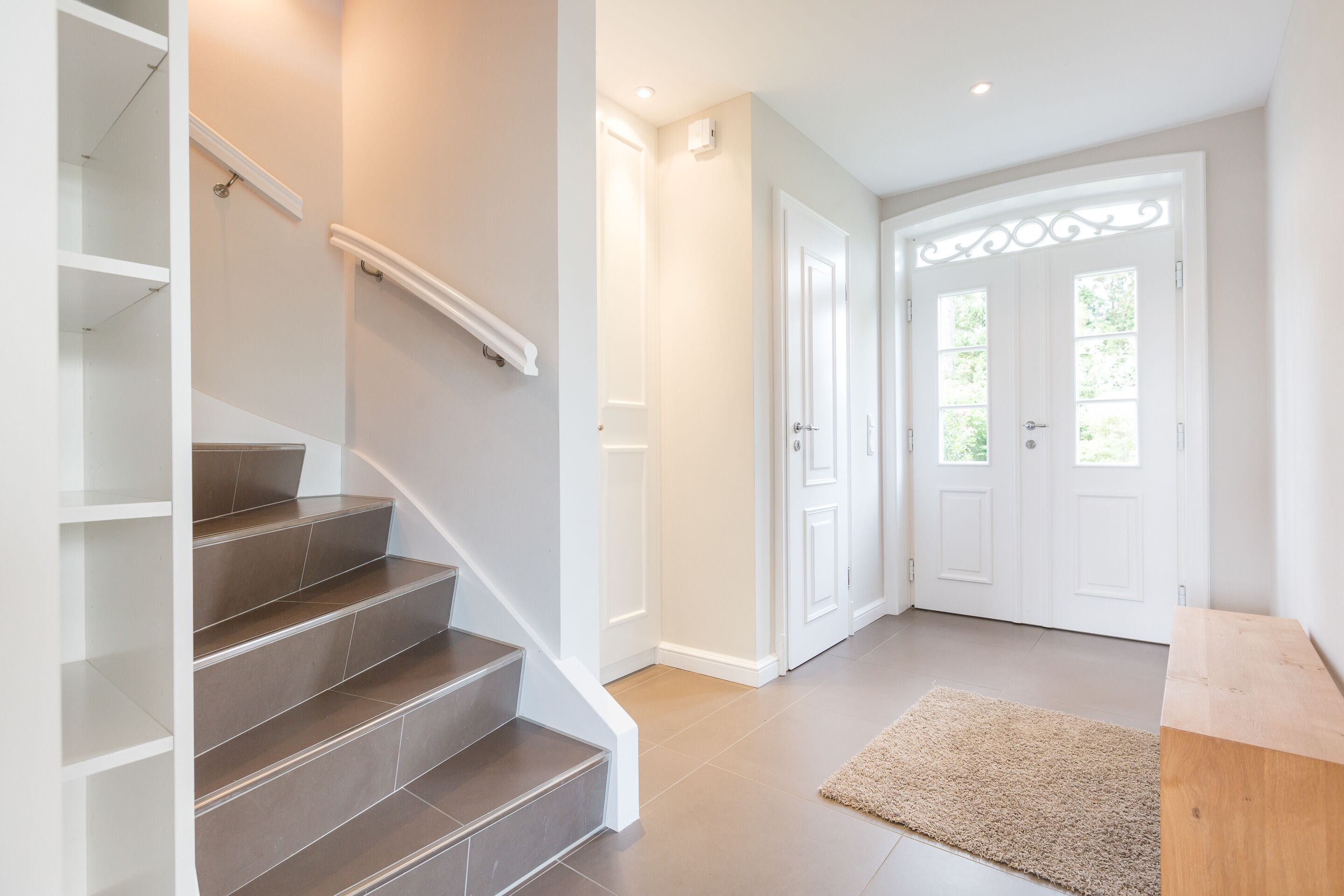 Eine Treppe mit Handlauf, die zu einer Zwischenebene führt, mit einer Holzbank und einem Teppich auf Fliesen.