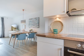 Una cocina moderna con encimera de madera, horno integrado y comedor con sillas azules y mesa de madera.