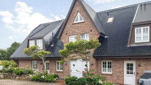 A two-story brick house with a steeply pitched roof, a small attached garage, and a paved driveway. - Appartement im Eg/ug mit ca. 76 qm Nutzfläche für bis zu 4 Personen (Wenningstedt-Braderup (Sylt))