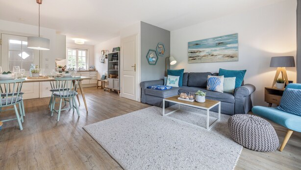 A modern living room with a grey sofa, a coffee table, and a dining area with a wooden table and chairs. - Appartement im Eg/ug mit ca. 76 qm Nutzfläche für bis zu 4 Personen (Wenningstedt-Braderup (Sylt))