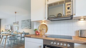 A modern kitchen with stainless steel appliances, a wooden countertop, and a dining area with a table set for four. - Appartement im Eg/ug mit ca. 76 qm Nutzfläche für bis zu 4 Personen (Wenningstedt-Braderup (Sylt))