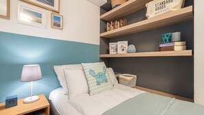 A neatly arranged bedroom with a bed, bedside lamp, and shelves with books and decorative items. - Appartement im Eg/ug mit ca. 76 qm Nutzfläche für bis zu 4 Personen (Wenningstedt-Braderup (Sylt))