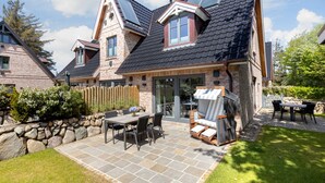 A house with a stone facade, a tiled roof, and a patio with outdoor furniture.