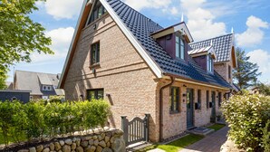 A two-story brick house with a steeply pitched roof, a stone wall, and a gated entrance.