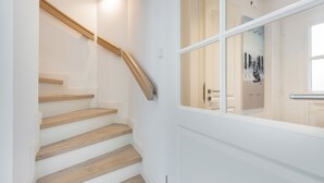 A staircase with wooden steps and a wooden handrail, leading to a white door with glass panels.