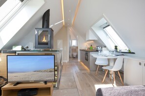 A modern loft bedroom with a large TV, a fireplace, and a skylight. - Design [&] Stil Pur. Raumwunder für Individualisten an den Tinnumer Wiesen (Sylt)