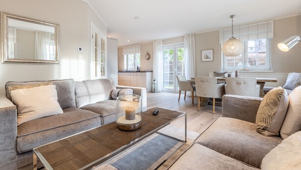 A modern living room with a sofa, a coffee table with a candle, and a dining area in the background.