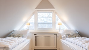 A bedroom with two beds, a window, a radiator, and a sloped ceiling.