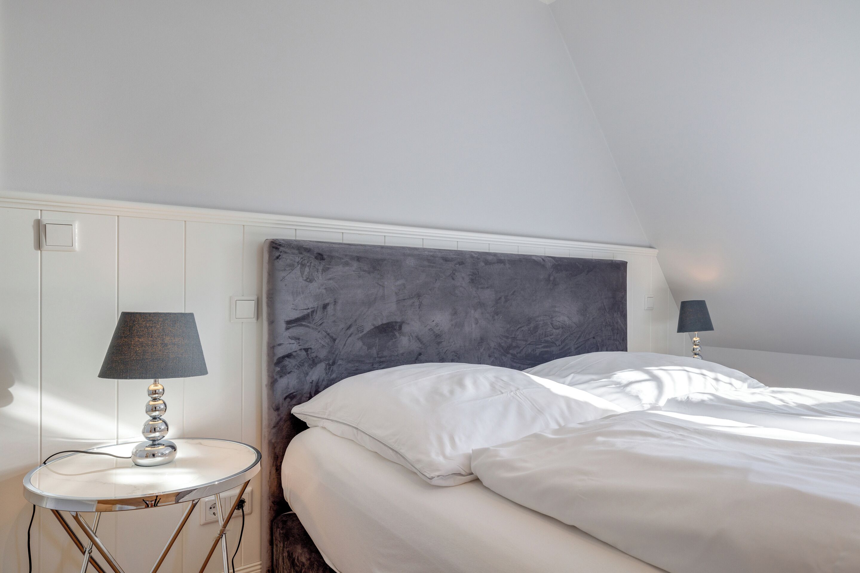 A bedroom with a bed, two bedside lamps, a round table, and a marble-patterned headboard.