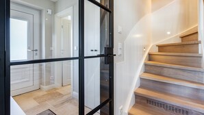 Ein modernes Interieur mit einer Treppe, die zu einer zweiten Etage führt, einem Glastür-Eingang und einem Flur mit einer Tür.