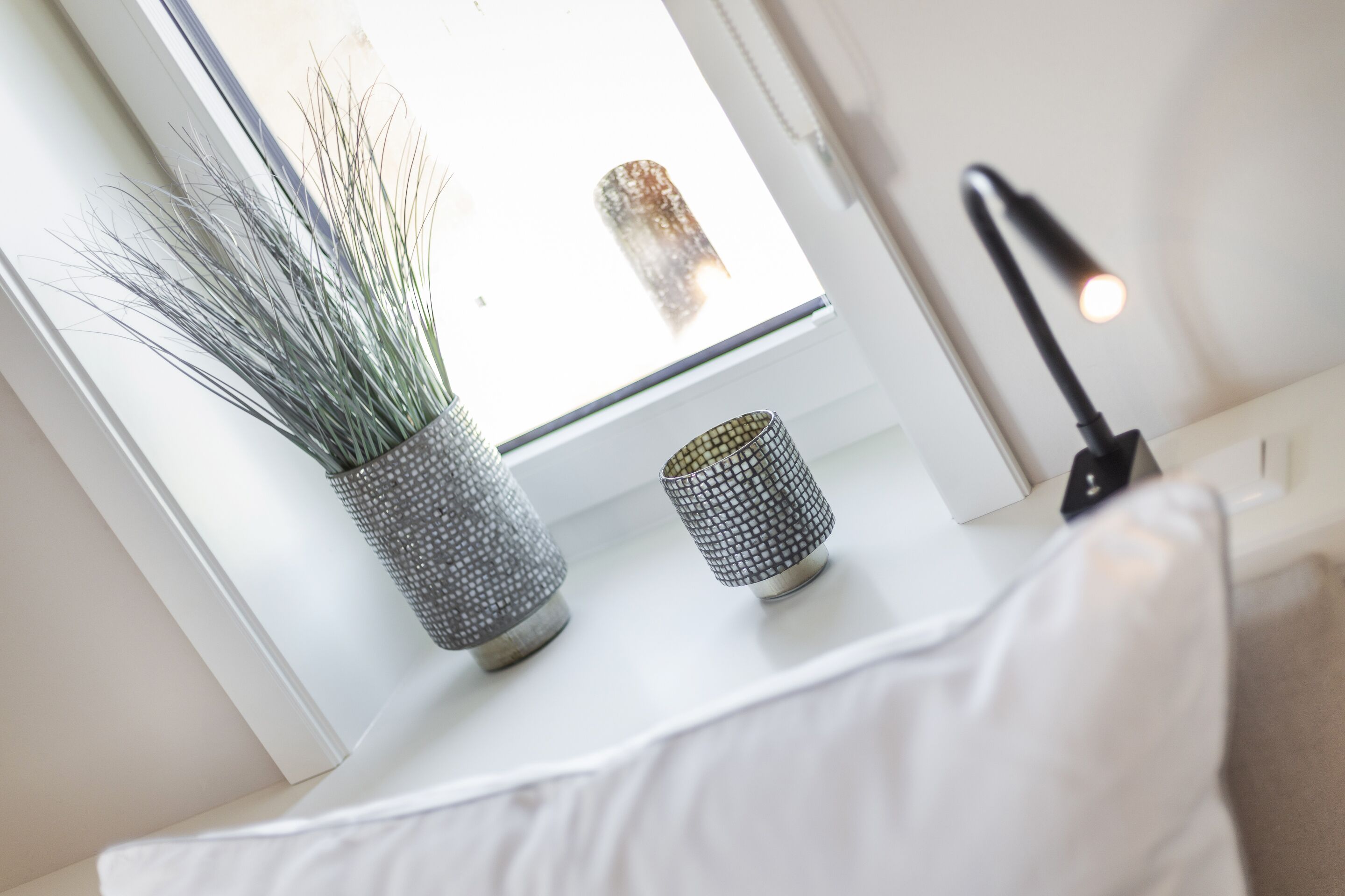 Et vindue med en plante og en lampe på en hvid overflade.