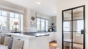 Eine moderne Küche mit weißen Schränken, einer schwarzen Arbeitsplatte und einem großen Fenster mit Blick ins Freie.