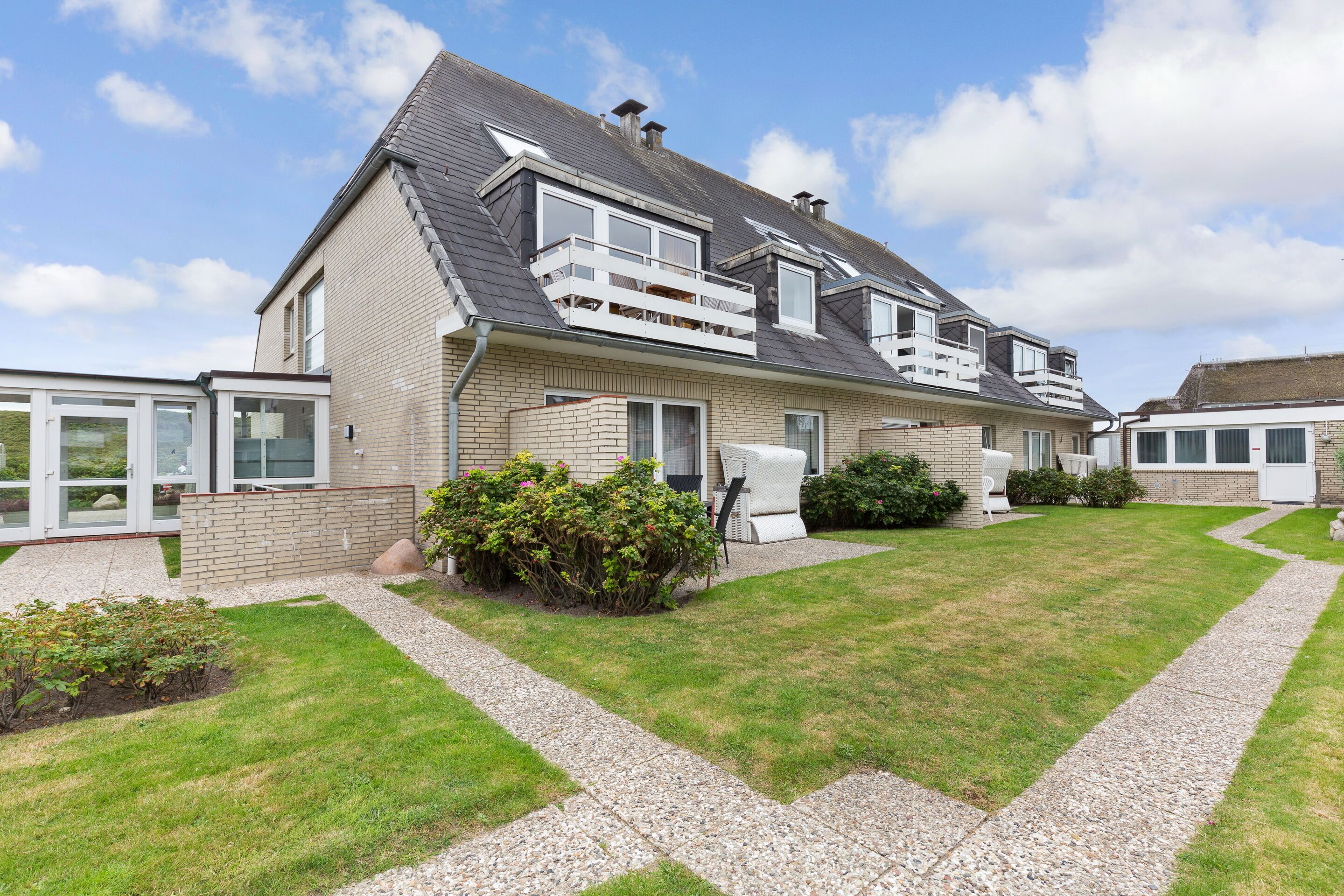 A two-story house with a sloped roof, a balcony, and a well-maintained lawn.