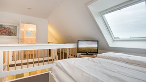 Makuuhuone, jossa on kalteva katto, sänky, televisio ja ikkuna, josta on näkymä.