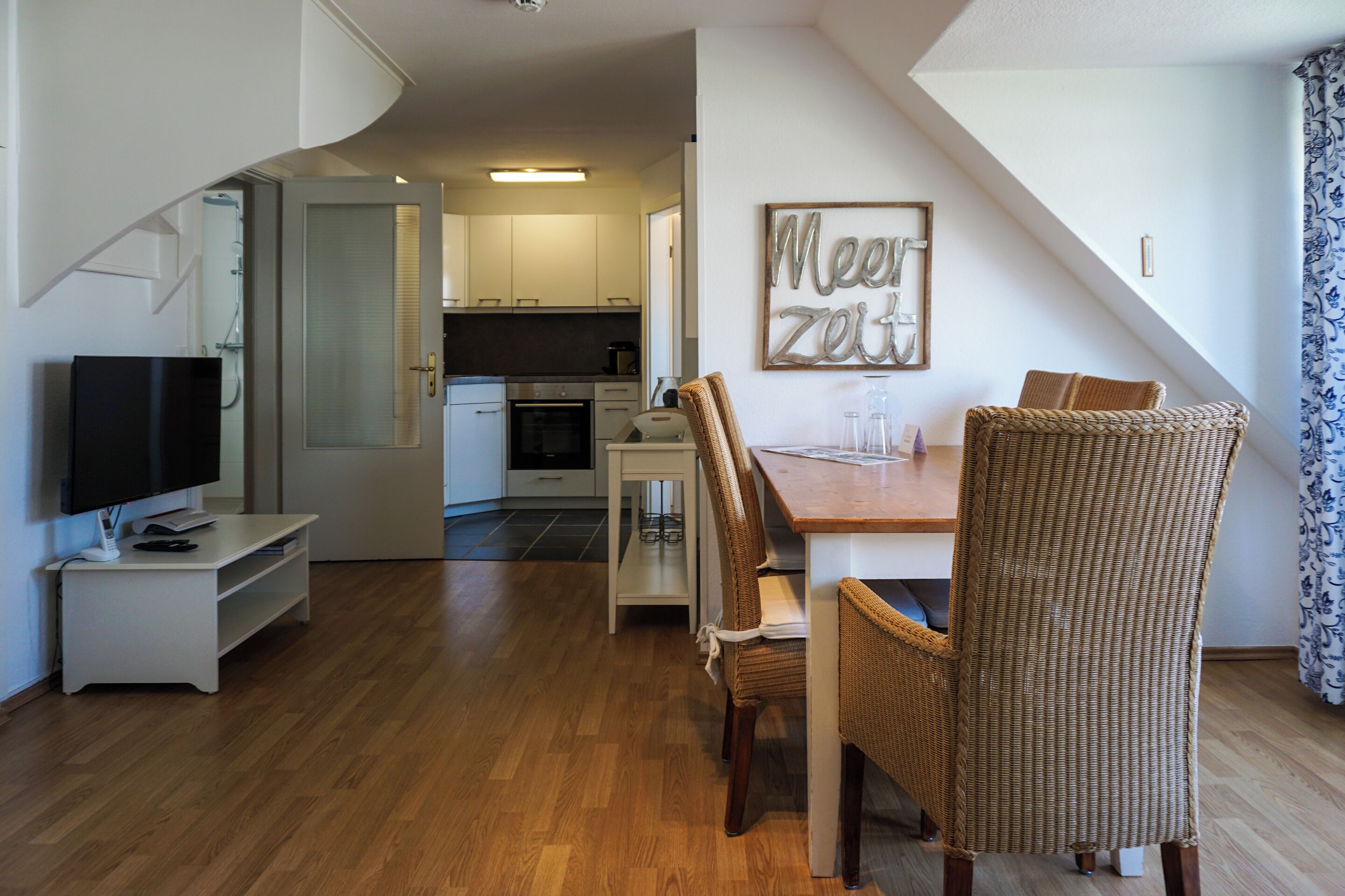 Een moderne woonkamer met een eetgedeelte, een televisie en een keuken op de achtergrond.