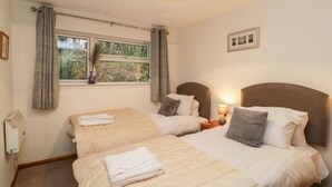 A hotel room with two beds, a window with curtains, a bedside lamp, and a framed picture on the wall. - Manorcombe 40 (Gunnislake)