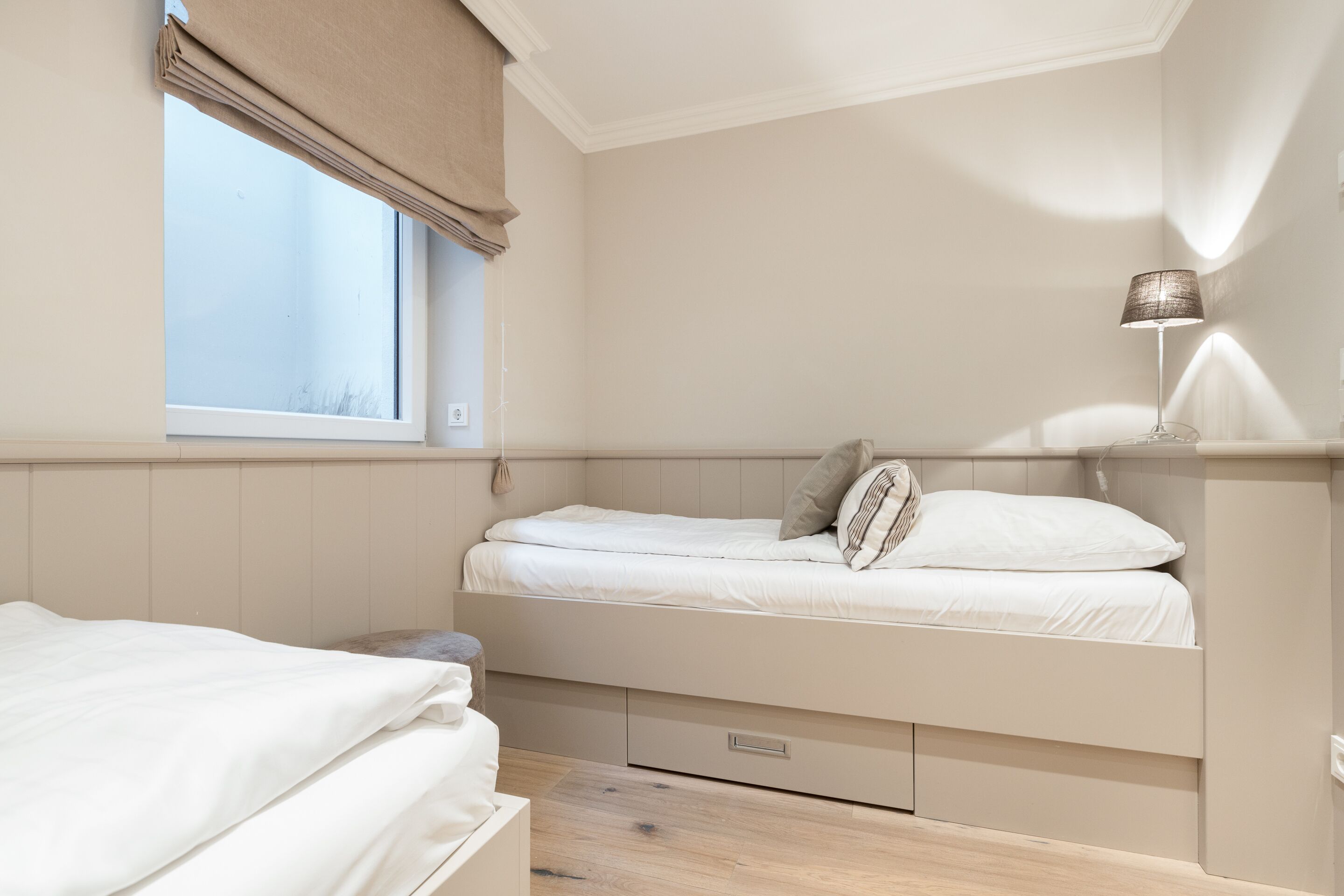 A bedroom with a single bed, a bedside table, a lamp, and a window with a curtain.