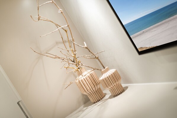 A wall-mounted television displaying a beach scene, a white shelf with two wooden vases, and a branch with dried leaves.