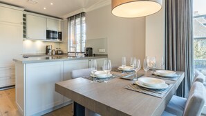 A modern kitchen with white cabinets, a central island, and a dining area set for four with glasses and plates. - Ferienwohnung "düün Hüs, Appartement Nr. 3" in Westerland, Sylt (Sylt)