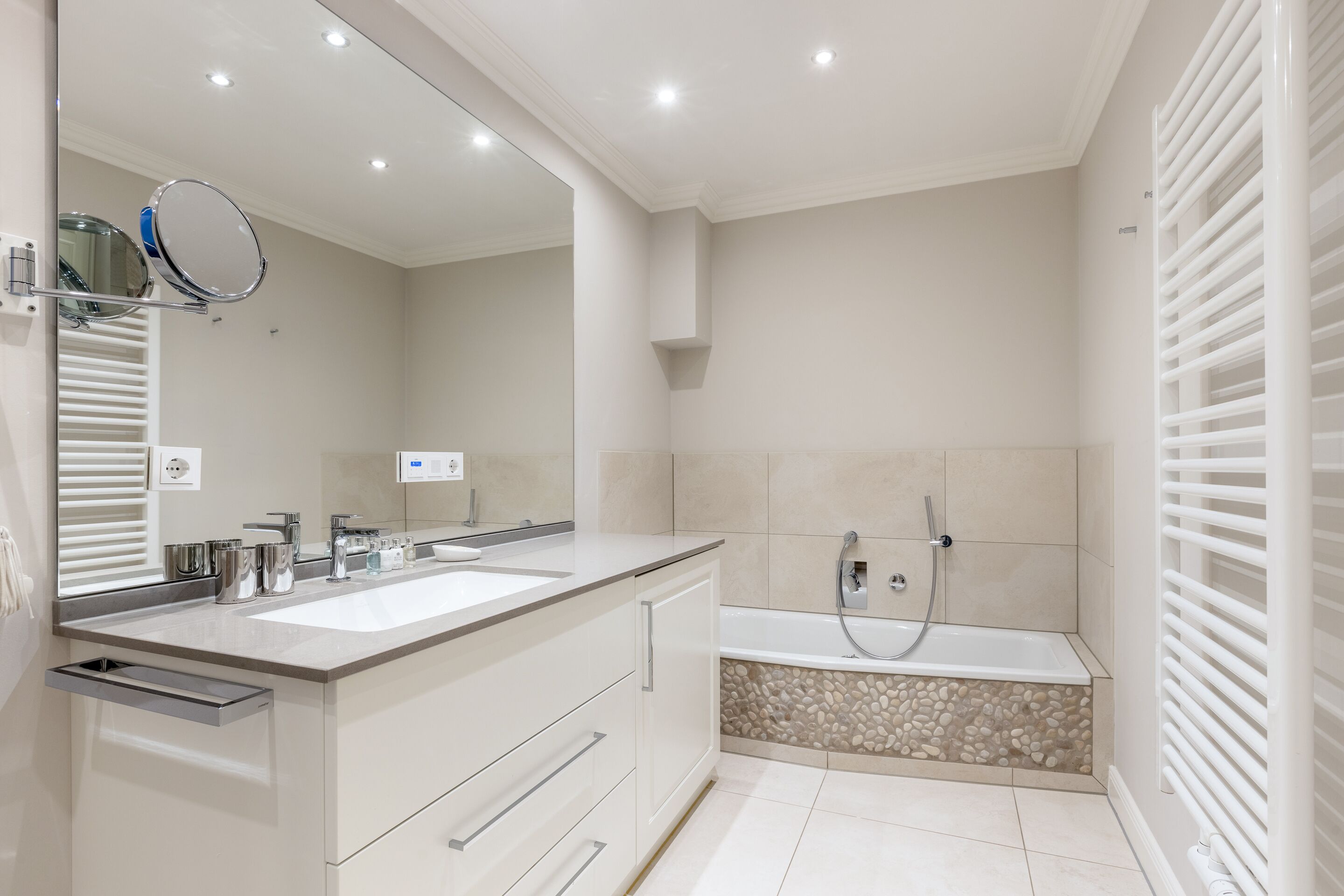 A modern bathroom with two sinks, a large mirror, a bathtub, and a towel rack.