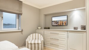 A bedroom with a bed, a chair, a TV mounted on the wall, and a window with a view of the sea. - Ferienwohnung "düün Hüs, Appartement Nr. 3" in Westerland, Sylt (Sylt)