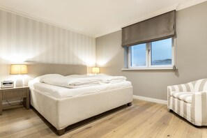 A bedroom with a bed, bedside lamps, a chair, and a window with a view. - Ferienwohnung "düün Hüs, Appartement Nr. 3" in Westerland, Sylt (Sylt)