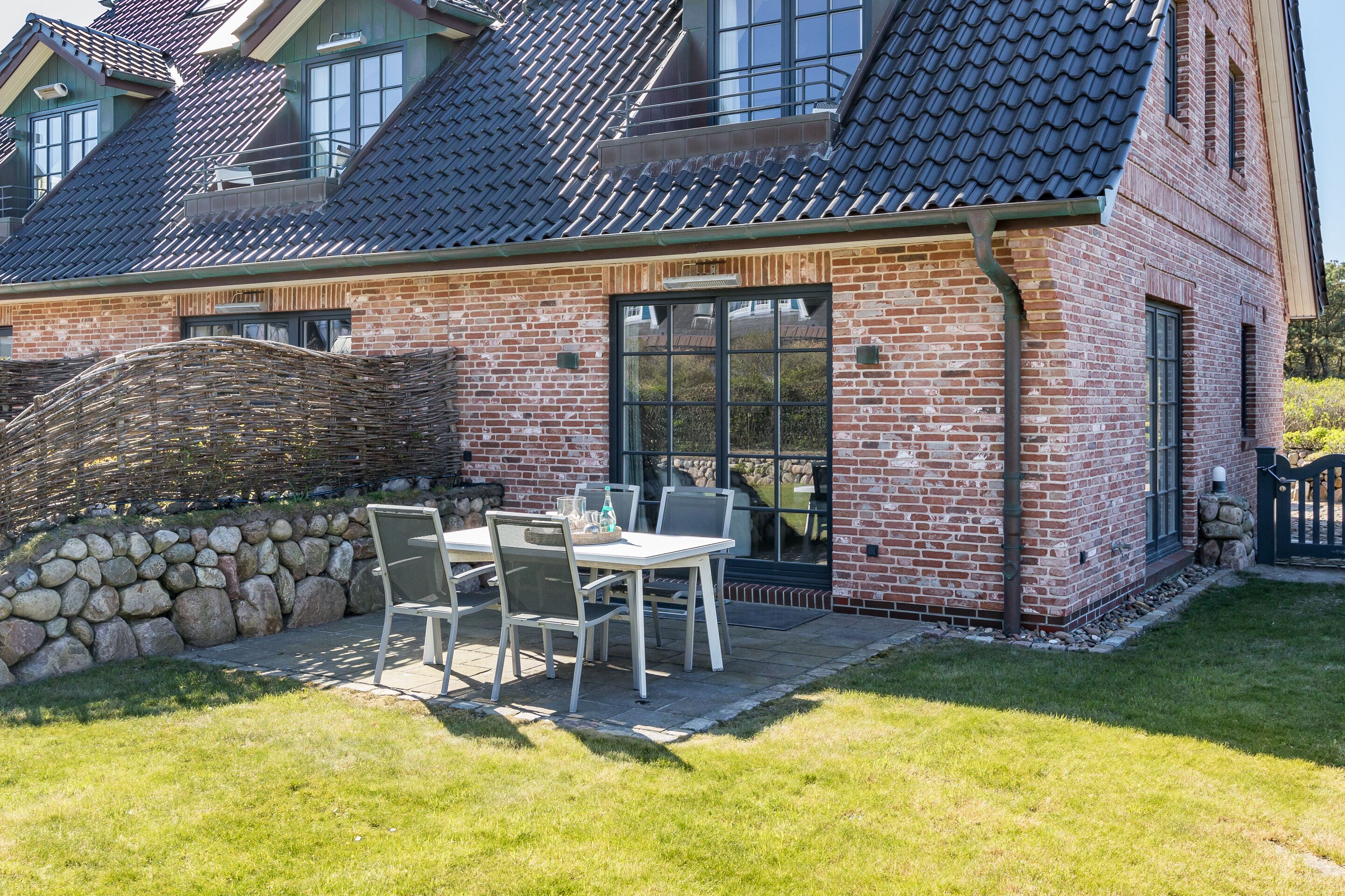 A brick house with a tiled roof, a stone wall, and a patio with a table and chairs.