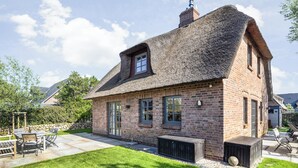 A brick house with a thatched roof, a patio with outdoor furniture, and a well-maintained lawn. - Das Traumhaus für Designliebhaber, Ästheten, Entschleuniger und Wahre Sylfans ! (Sylt)