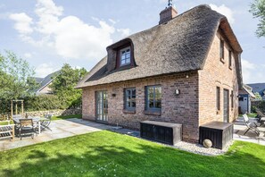 A brick house with a thatched roof, a patio with outdoor furniture, and a well-maintained lawn. - Das Traumhaus für Designliebhaber, Ästheten, Entschleuniger und Wahre Sylfans ! (Sylt)