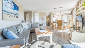 A modern living room with a grey sofa, a wooden coffee table, and a painting of a beach scene.