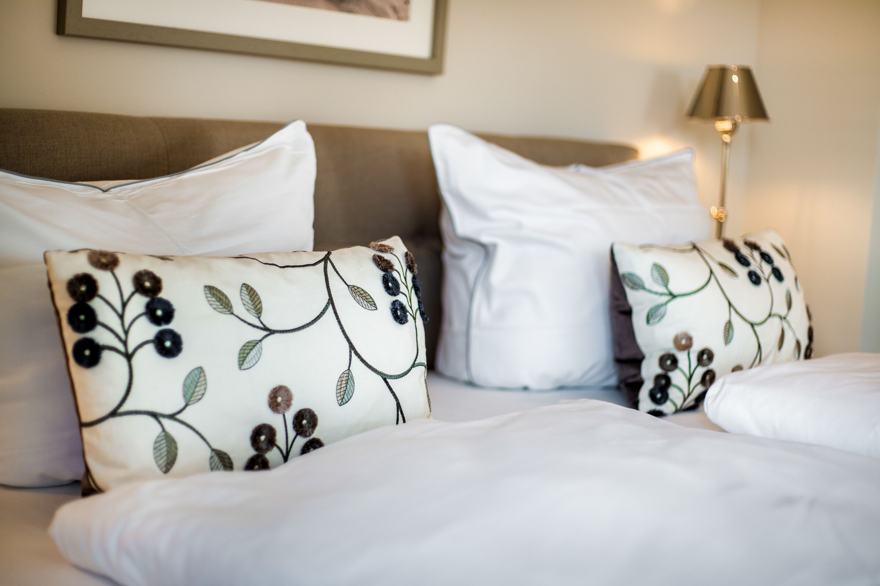 A neatly made bed with white linens and decorative pillows featuring a floral pattern.