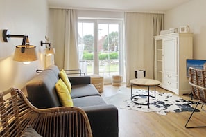 Una sala moderna con un sofá, una silla de mimbre, una mesita redonda y un aparador.