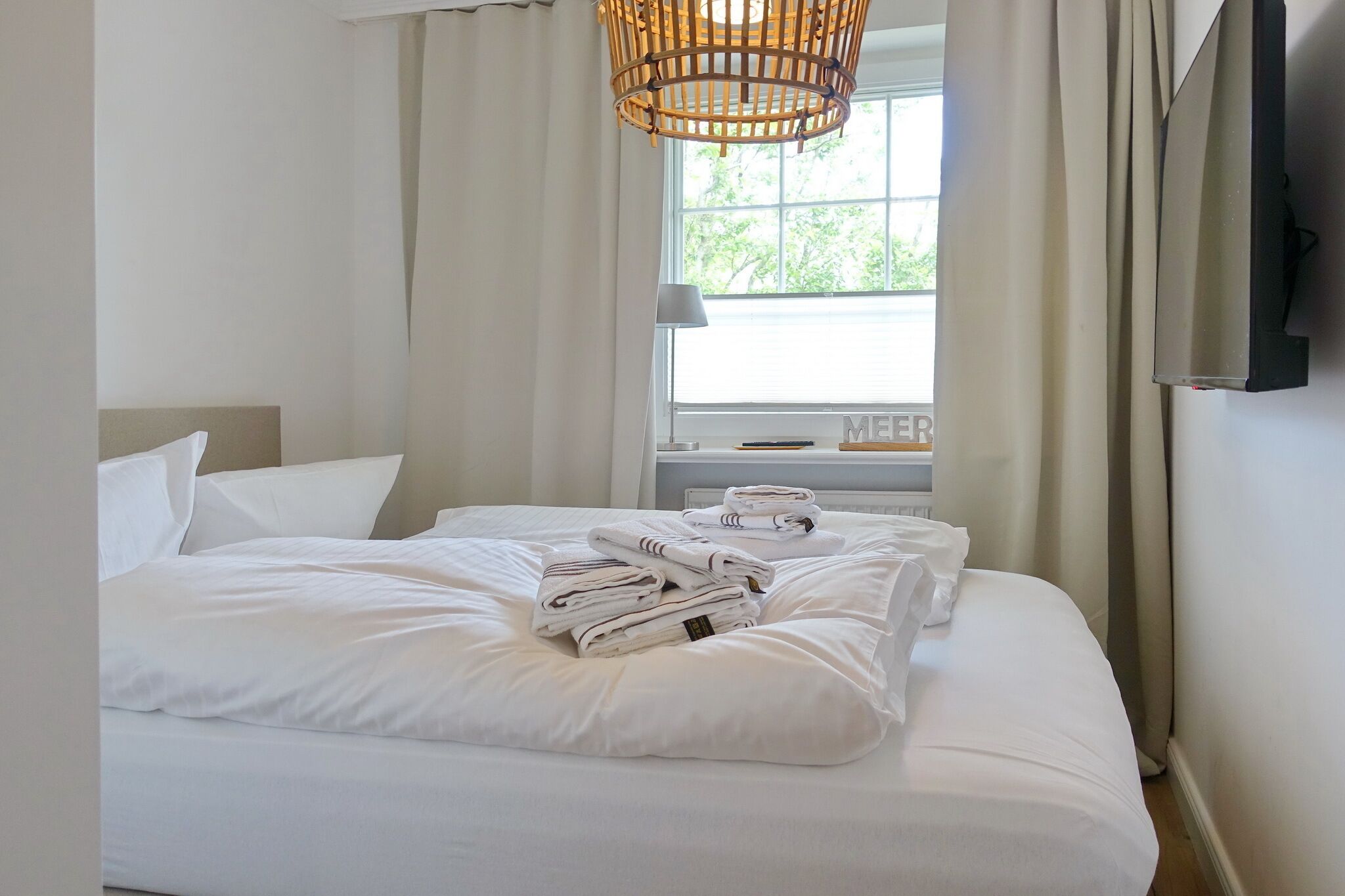 A hotel room with a neatly made bed, a television mounted on the wall, and a window with curtains.