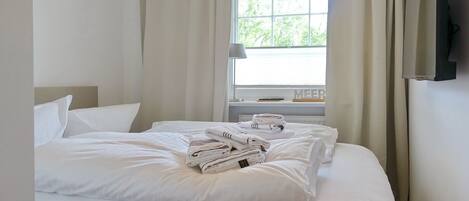 A hotel room with a neatly made bed, a television mounted on the wall, and a window with curtains.