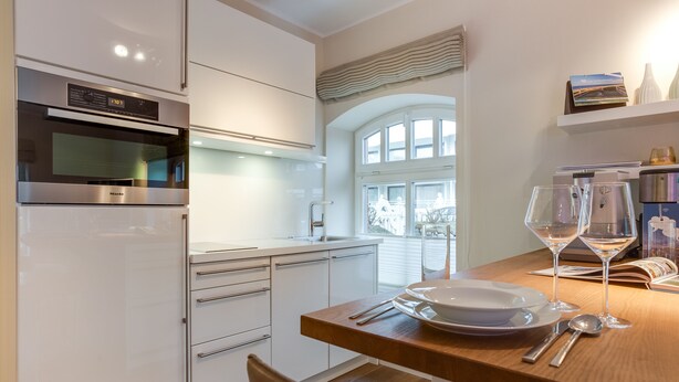 Eine moderne Küche mit weißen Schränken, einem eingebauten Backofen und einer Essecke mit einem Holztisch, gedeckt für zwei Personen.
