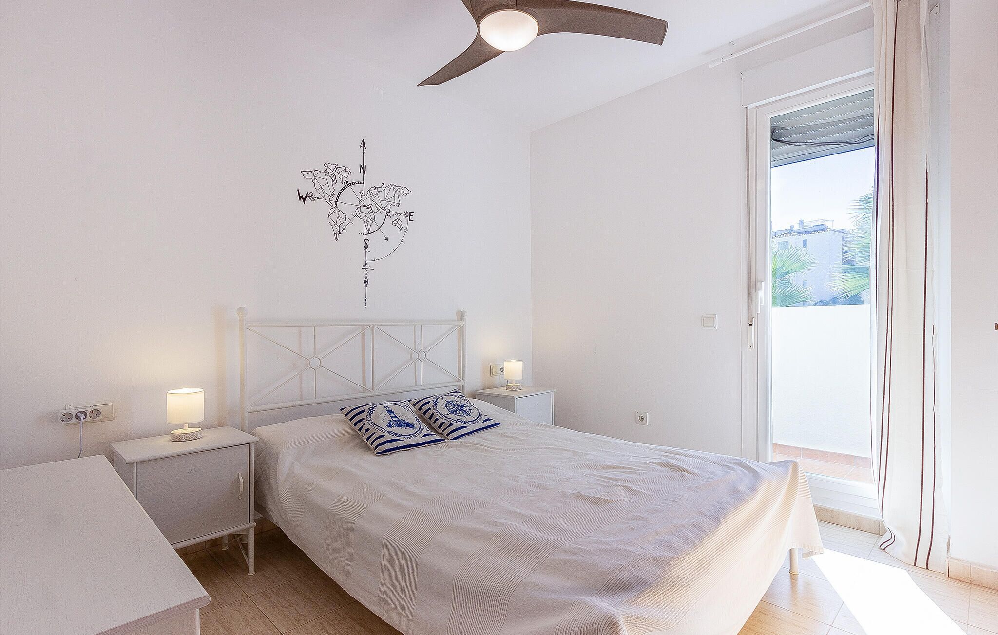 Ein Schlafzimmer mit Bett, Nachttischen, Deckenventilator, Fenster mit Blick und Wanddekoration.