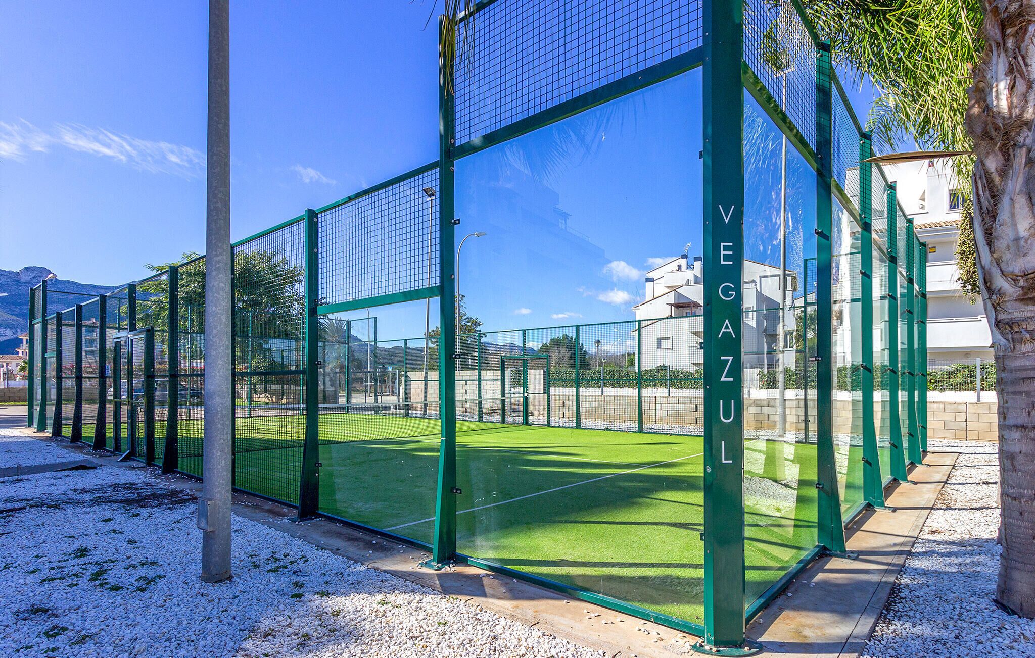 A tennis court with a green fence and a clear sky.