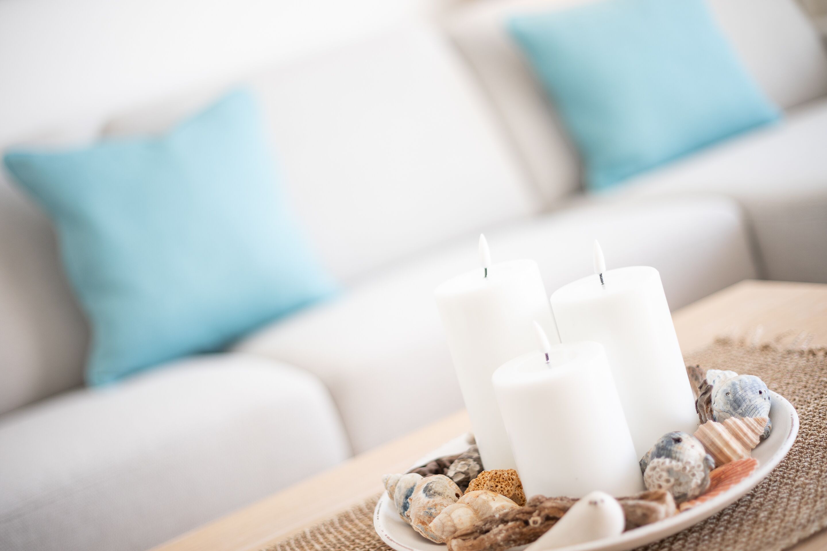 Un canapé blanc avec des coussins bleu clair, un porte-bougie blanc avec trois bougies et une assiette remplie de pierres décoratives.