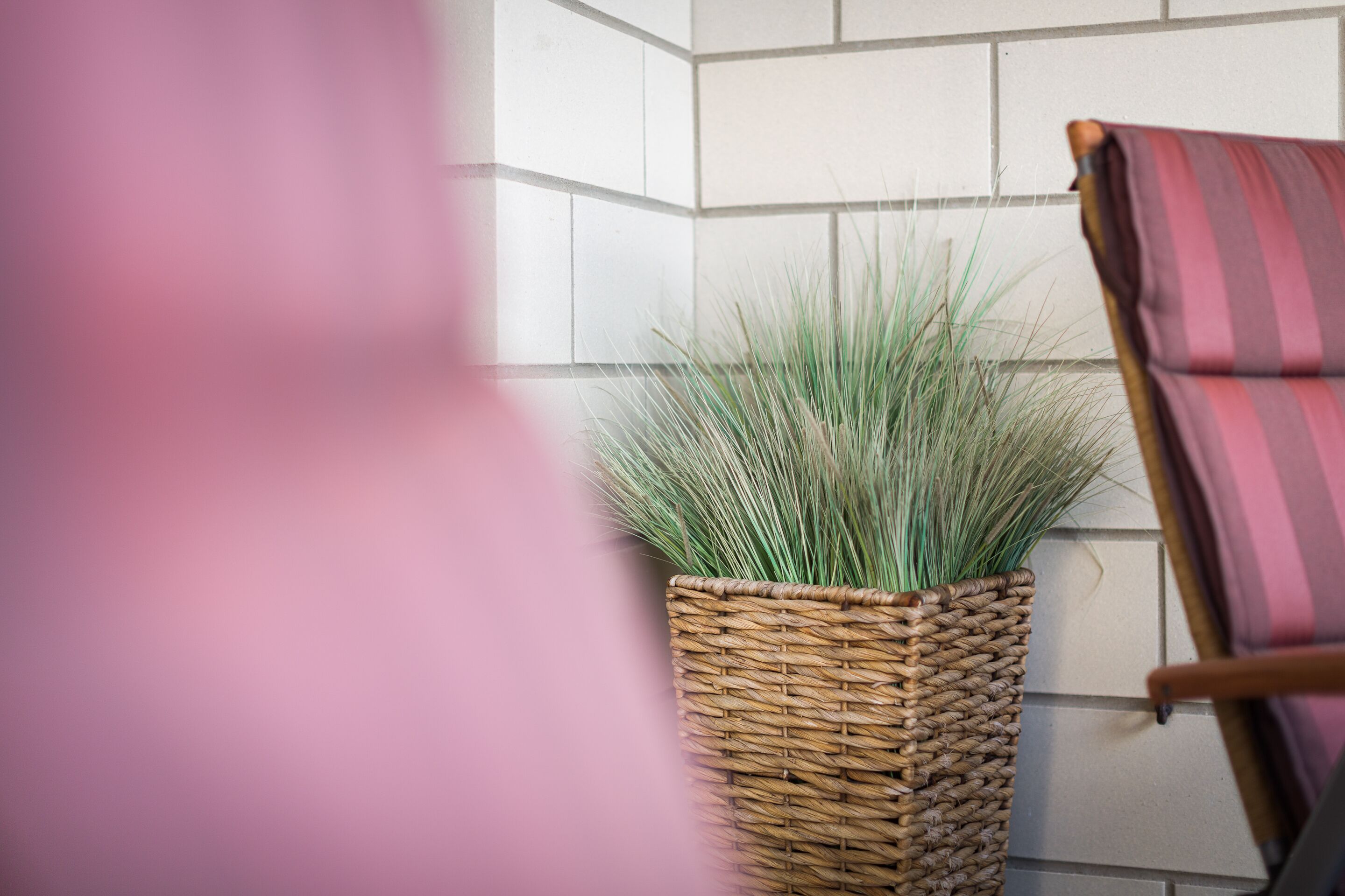 Un pot en osier contenant de l’herbe verte, adossé à un mur carrelé.