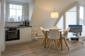 A modern kitchen with a dining area, featuring a built-in oven, a coffee maker, and a TV on a stand.