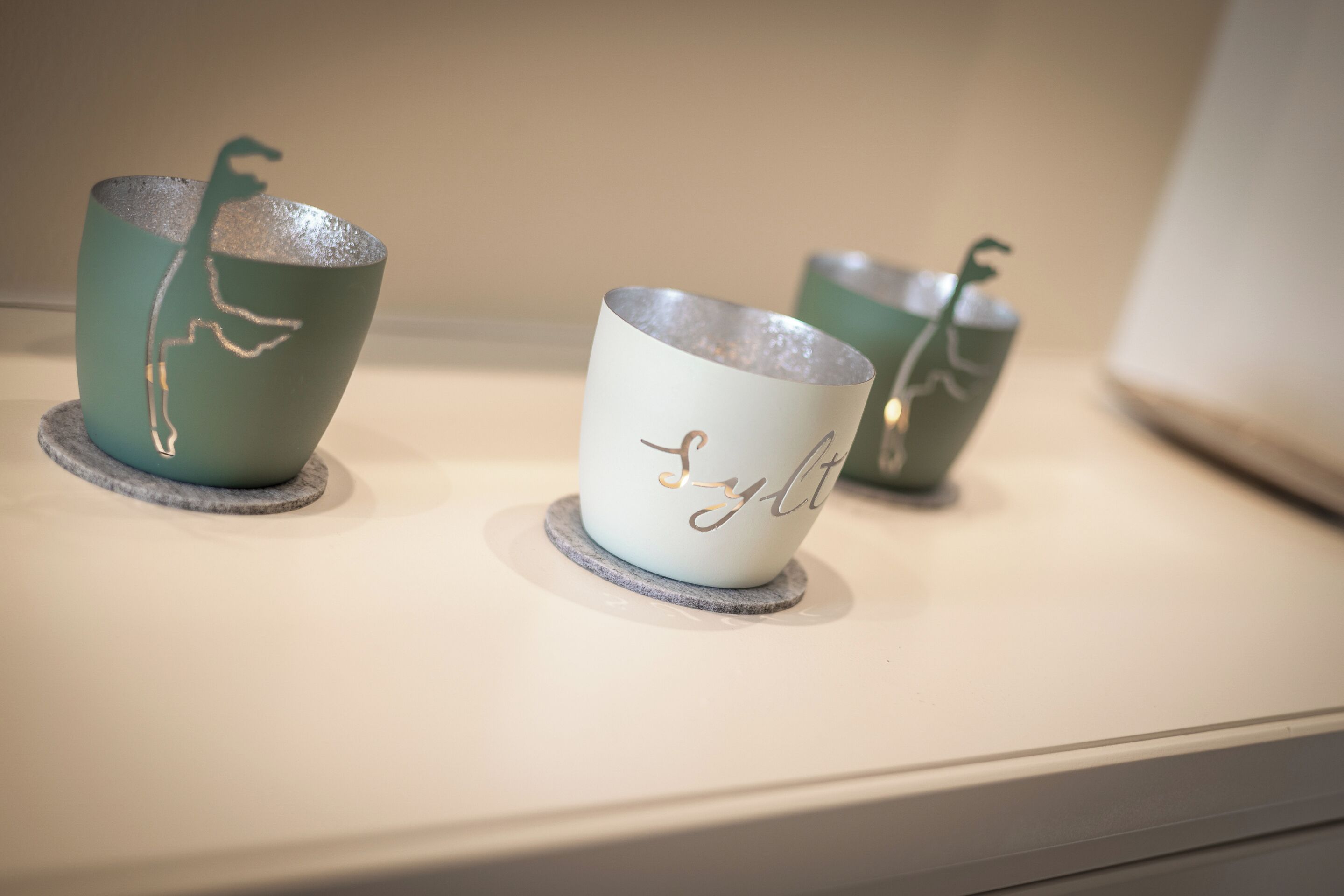 Three ceramic cups with a plant design on a shelf.