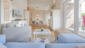 A modern living room with a sofa, a coffee table, and a dining area in the background. - Das Appartement Senskin für 2 Personen in Ruhiger Lage in Westerland (Sylt)